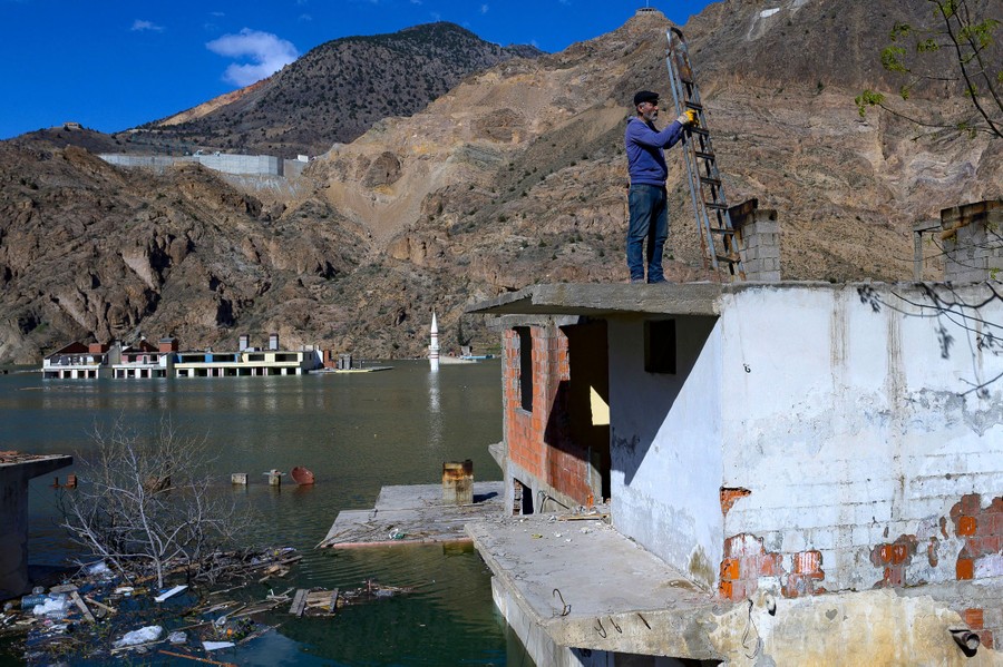 A person holds a ladder atop a partially flooded building.