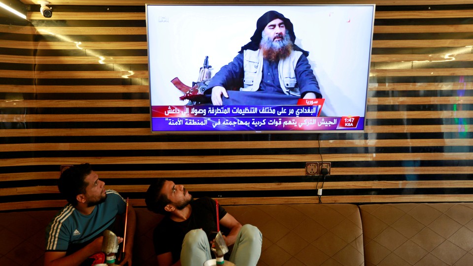 Two Iraqi youths stare at a TV showing an image of Abu Bakr al-Baghdadi.