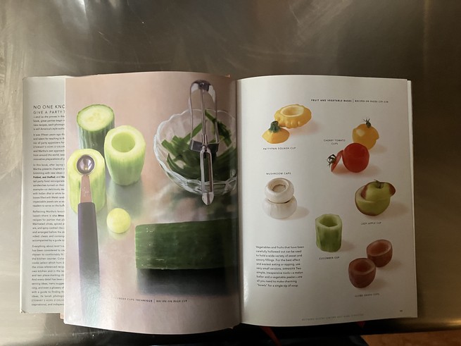 Martha Stewart-boek, opengeslagen op een metalen toonbank.  Pagina's tonen een uitgeholde komkommer en ander uitgeschept fruit en groenten, waaronder een druif.