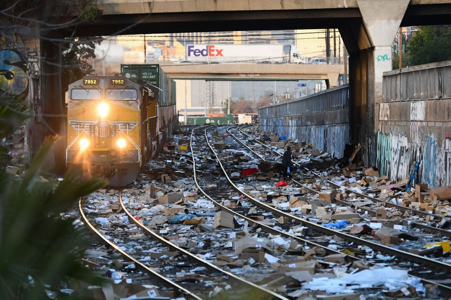 A train passes below a bridge, amid the debris of thousands of opened packages and boxes strewn across the tracks.