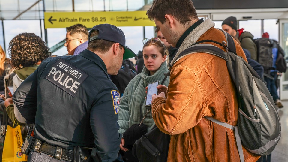 A traveler shows a police officer something on his phone while standing in line at an airport