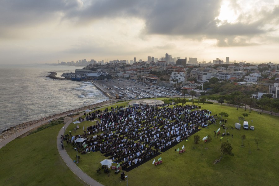 A crowd of people gather in rows in a seaside park to offer prayers.