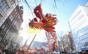 A crowd gathers in a street watching performers move a large dragon puppet around.