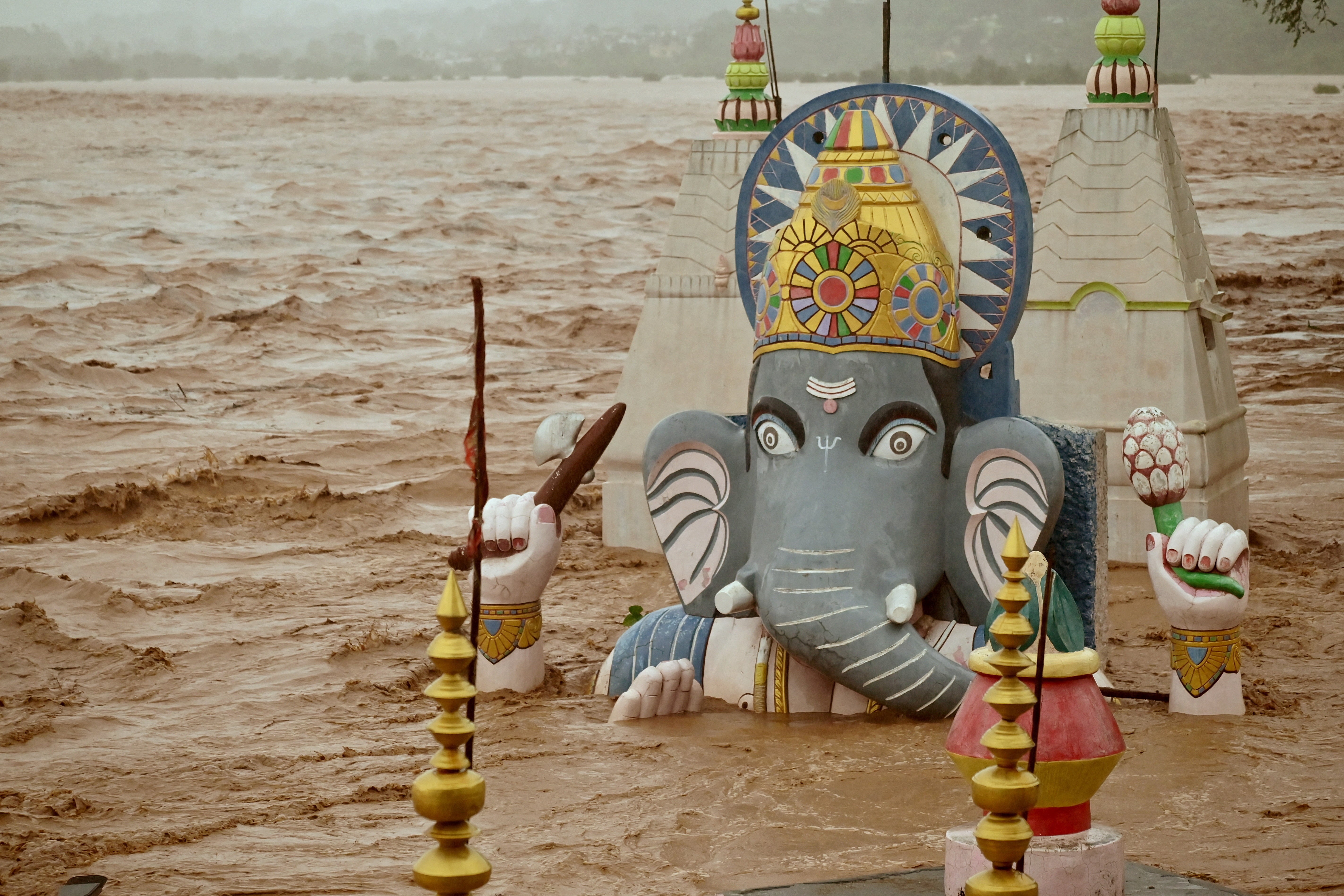 Rushing floodwater surrounds and passes by a statue of a Hindu god.