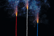 photo-illustration of red, white, blue lit fuses burning and smoking on black background