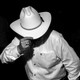 A man in a white shirt tilts the brim of a cowboy hat downward.
