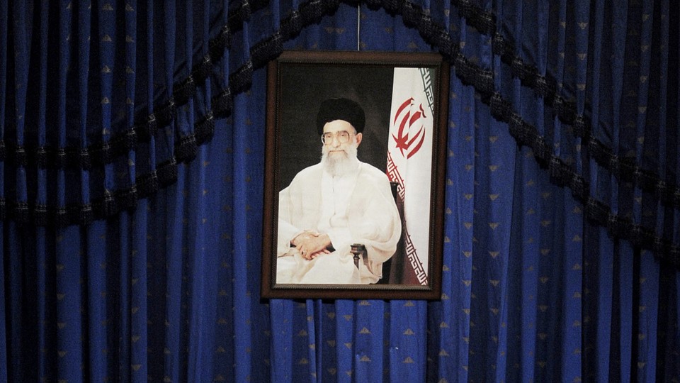 A portrait of Khamenei hangs against a blue curtain.