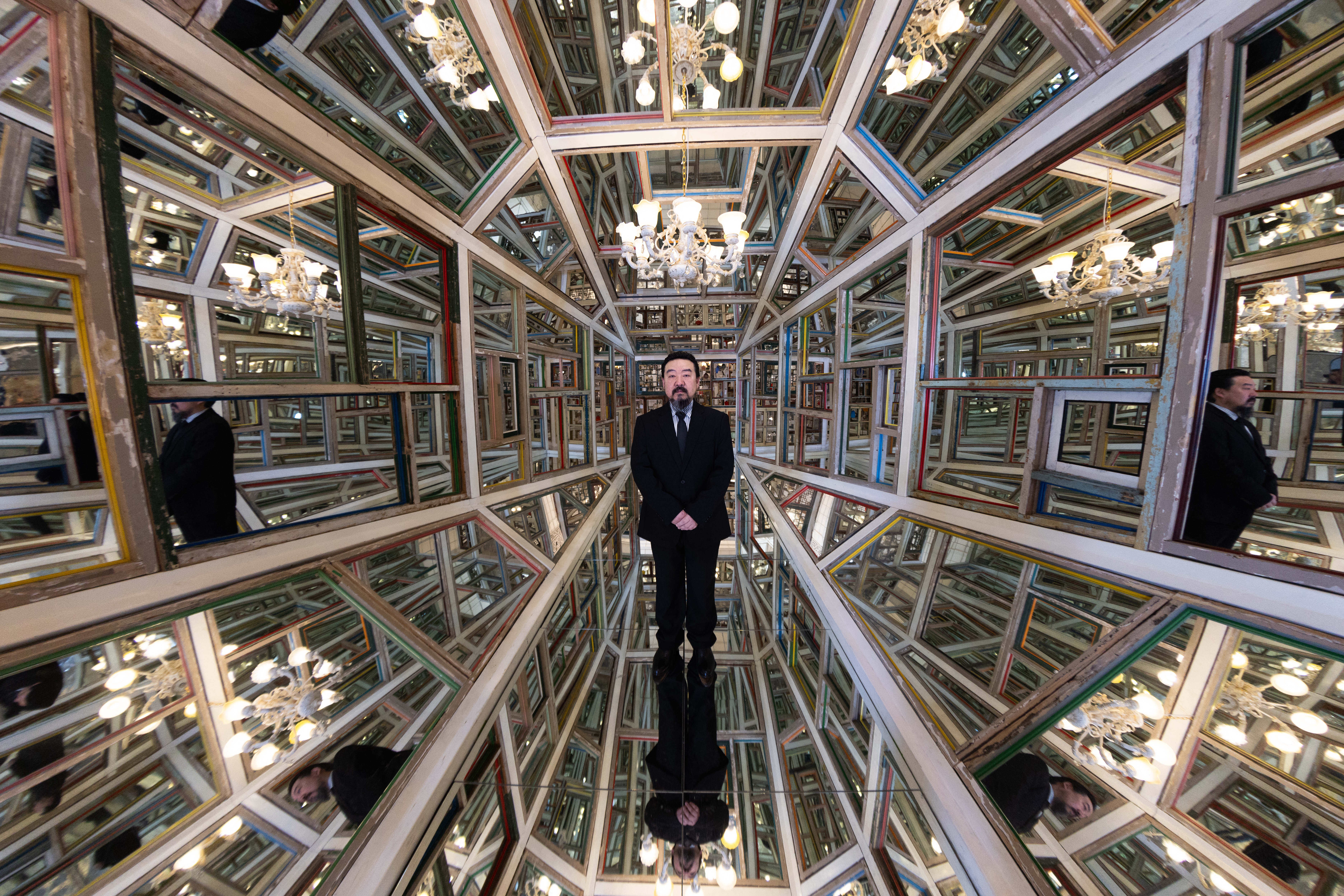 An artist poses inside an intricate hall of mirrors installation.