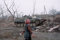 A women walks past a tank and ruins.