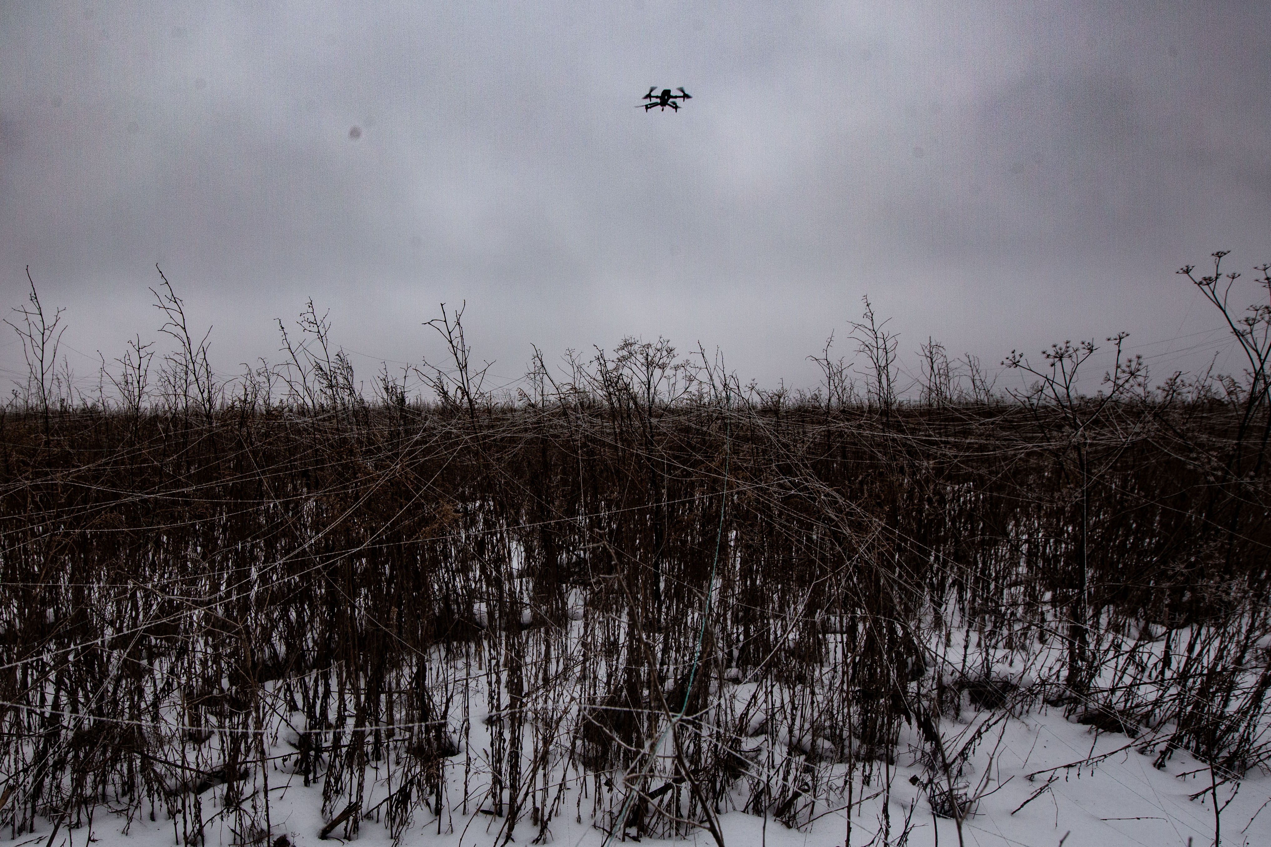A drone flies over a field littered with fiber-optic drone cables.