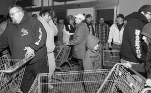 Customers push shopping carts while crowded in a small room.