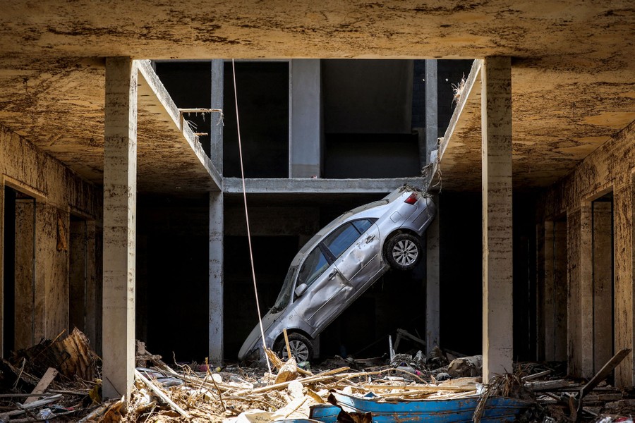 A wrecked car, tossed by a flood, rests at a sharp angle amid other flood debris in a building.