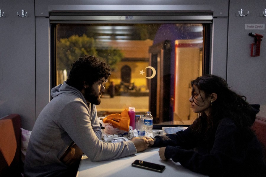 A couple holds hands while sitting inside a train carriage.