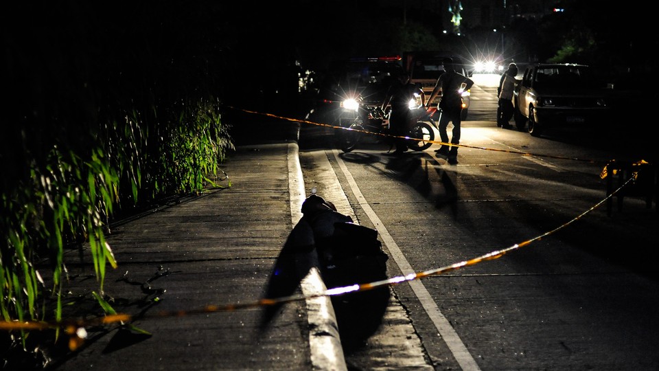 An alleged drug dealer and victim of a summary execution with his head wrapped in tape is examined by police on July 27, 2016, in Manila, Philippines.