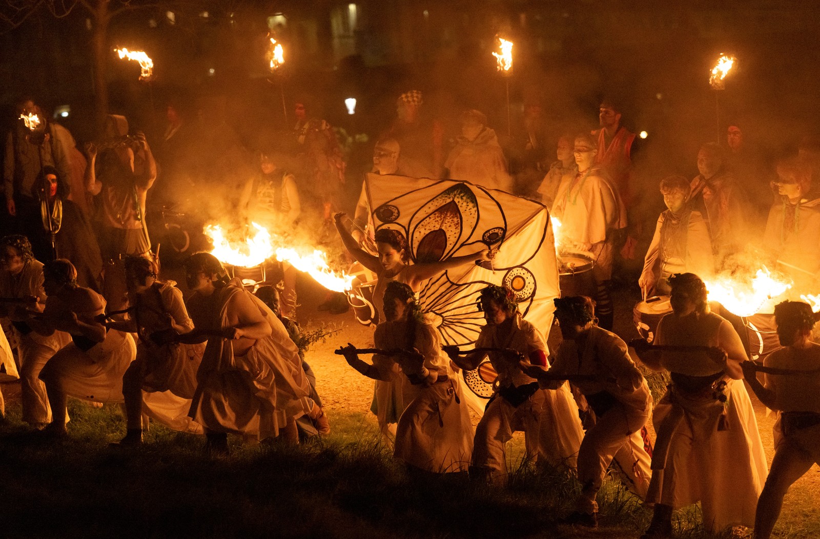Performers in traditional pagan costumes, some with torches attached to rigs, dance at night.