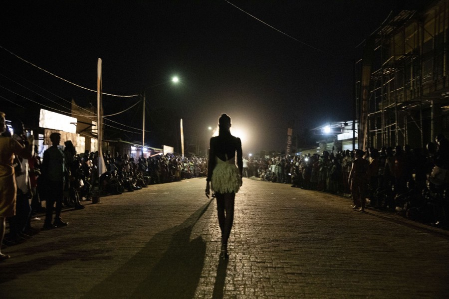 Models walk down the center of a street at night, with onlookers standing on either side.