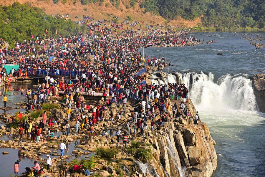 A large crowd of people gathers on rocks along a waterfall.