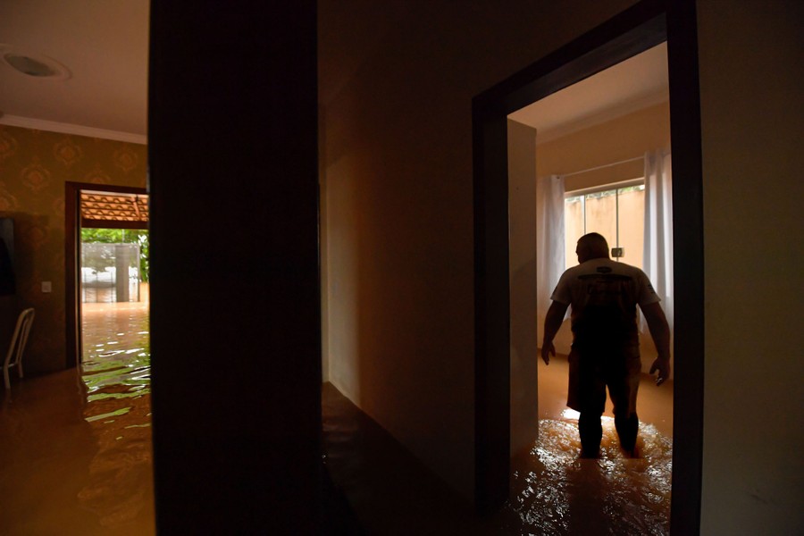 A person wades through knee-deep floodwater in their home.