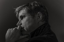 A black-and-white profile portrait of the writer Daniel Kehlmann in Berlin, his hand raised to his chin.