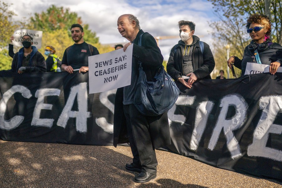 Several people attend a protest, holding up signs that read "Jews say: Ceasefire now."