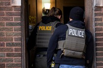 Photo of two agents wearing vests labeled “POLICE” entering an apartment building