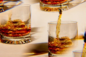 photo of brown liquor being poured over ice into multiple highball glasses