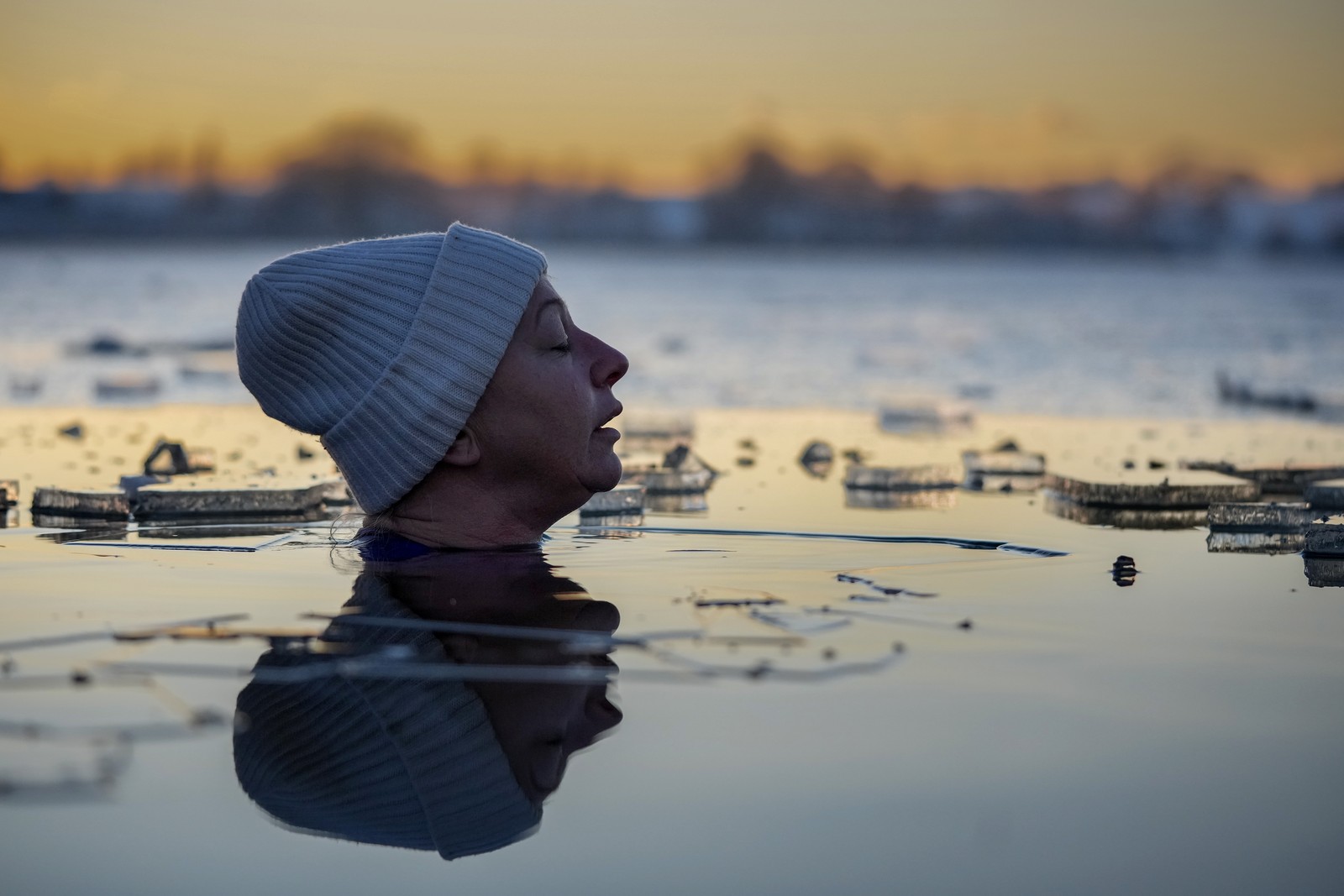 A close view of the head of a swimmer fully immersed in a lake, surrounded by ice