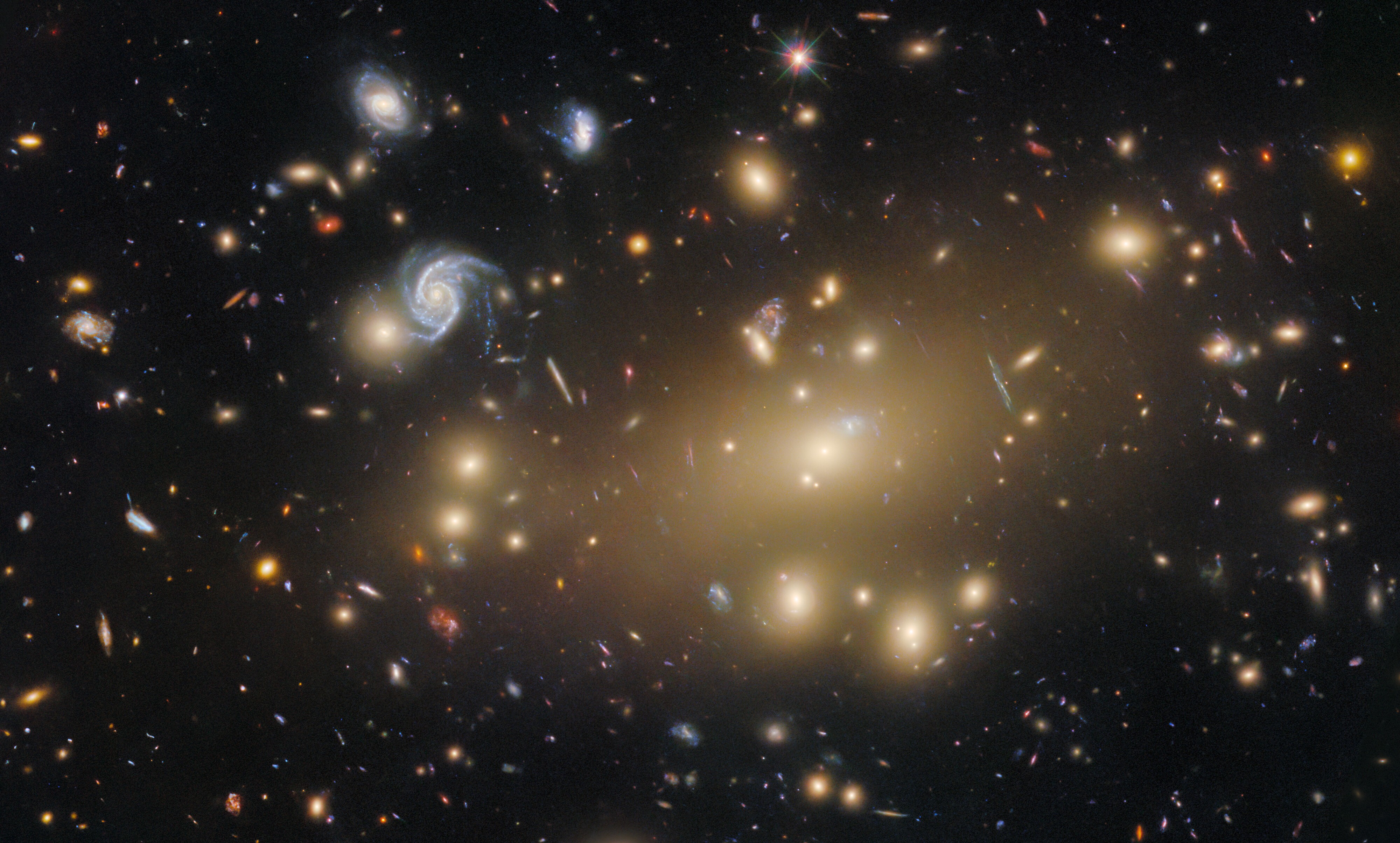 A deep-space image of many dozens of different-colored galaxies, some with a typical spiral shape, most appearing as small blobs of light.