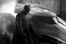 Black-and-white photo of Ben Affleck playing Batman, standing next to the Batmobile