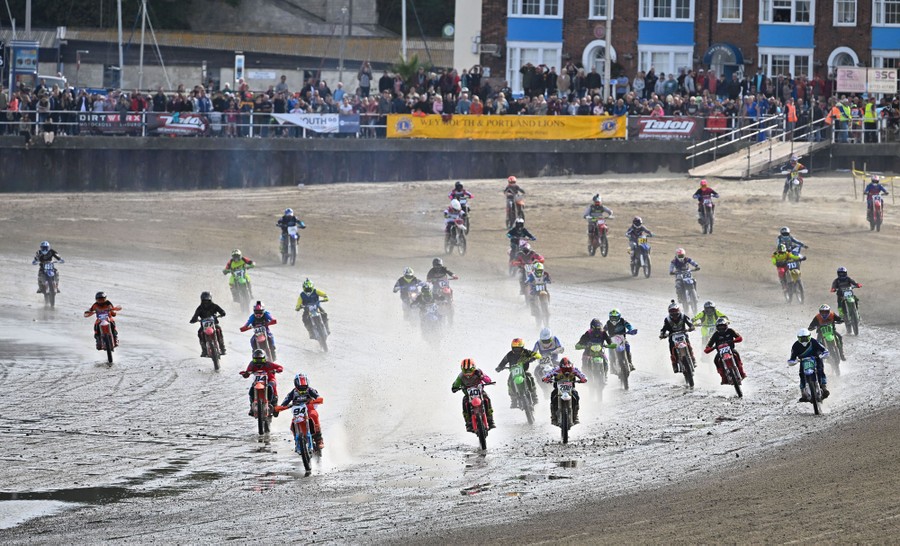 Dozens of motorcyclists race on a beach.