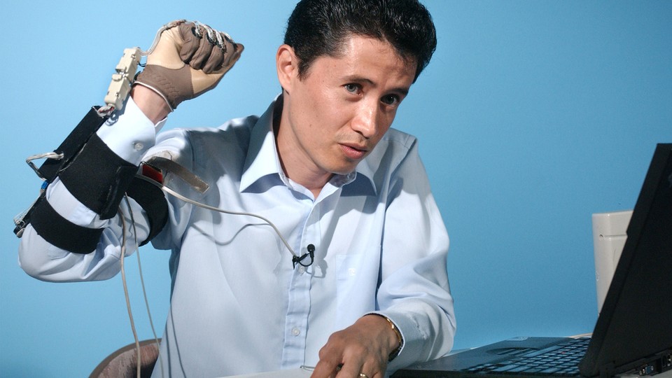 A man raises his hand, which is covered in a glove and wires