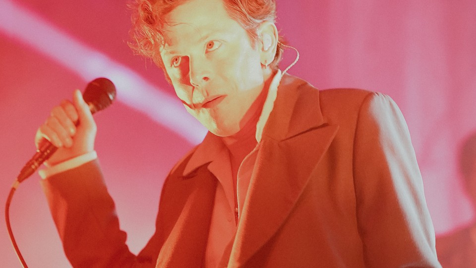 Mike Hadreas, a.k.a. Perfume Genius, onstage with a mic in his hand, bathed in red-pink light
