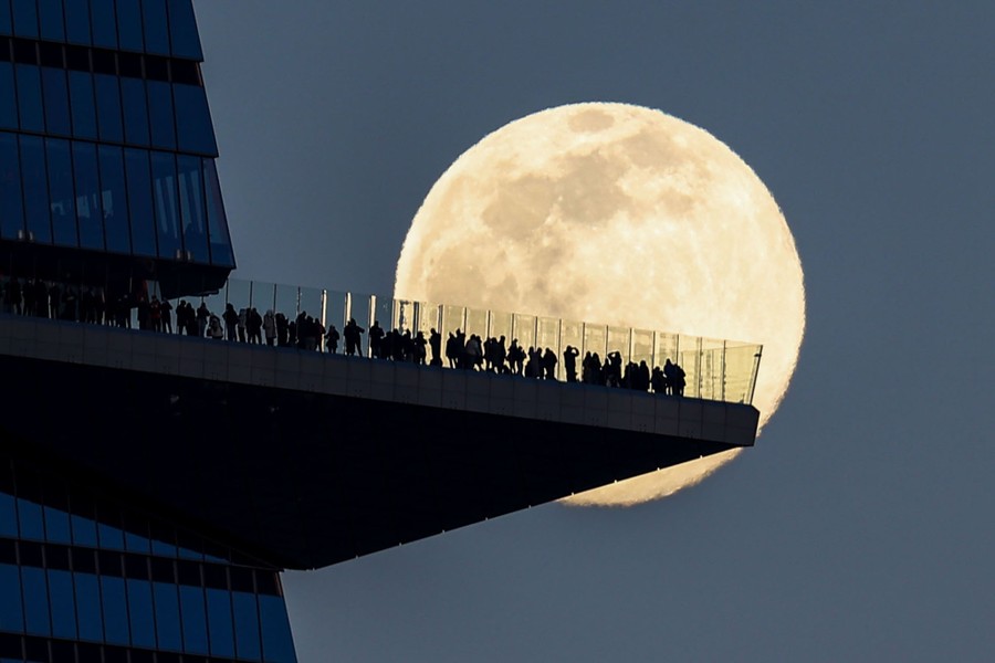 A full moon is seen behind a crowd of people standing on an observation deck.