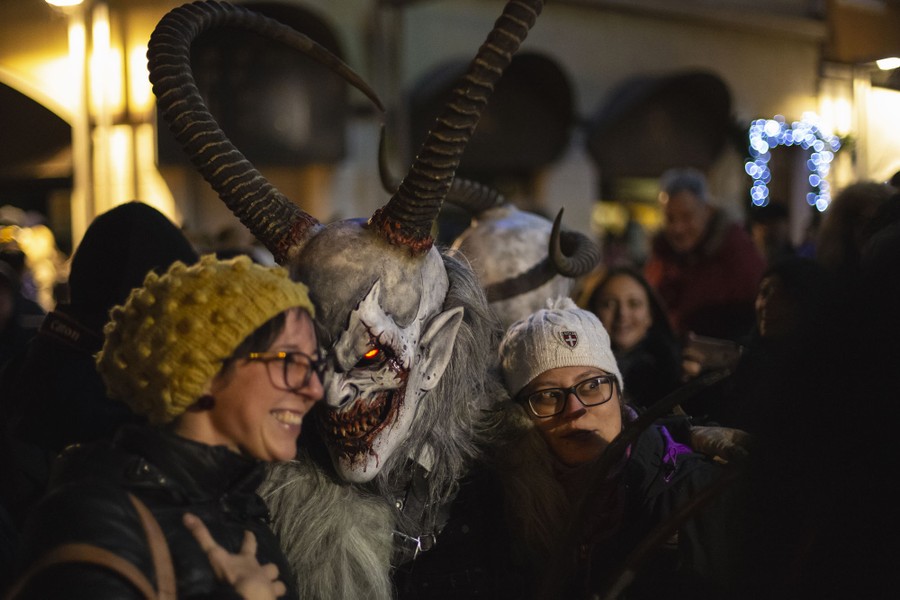 Smiling people pose with a performer wearing a frightening Krampus mask.
