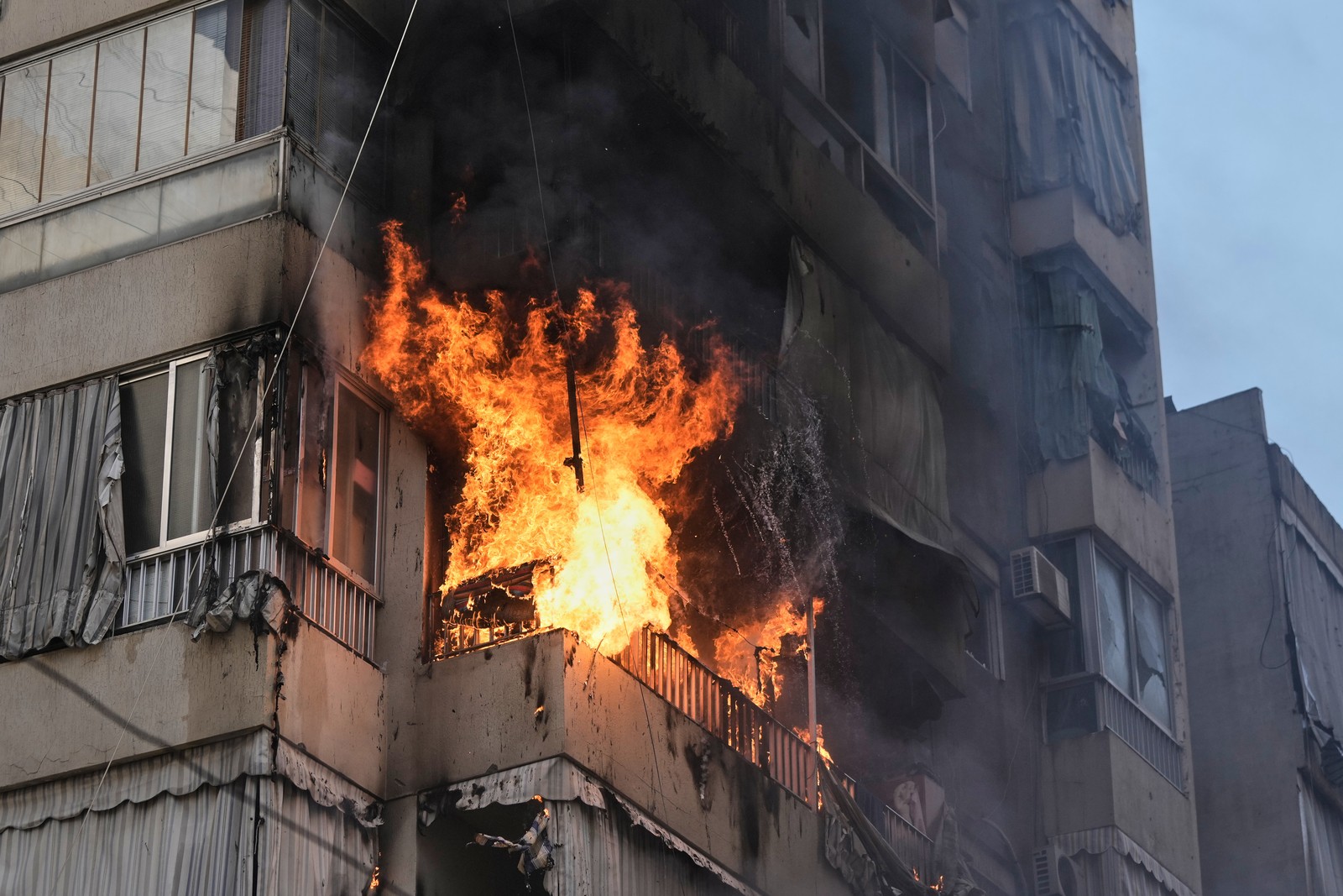 Smoke and flame rise from a balcony on a tall residential building.