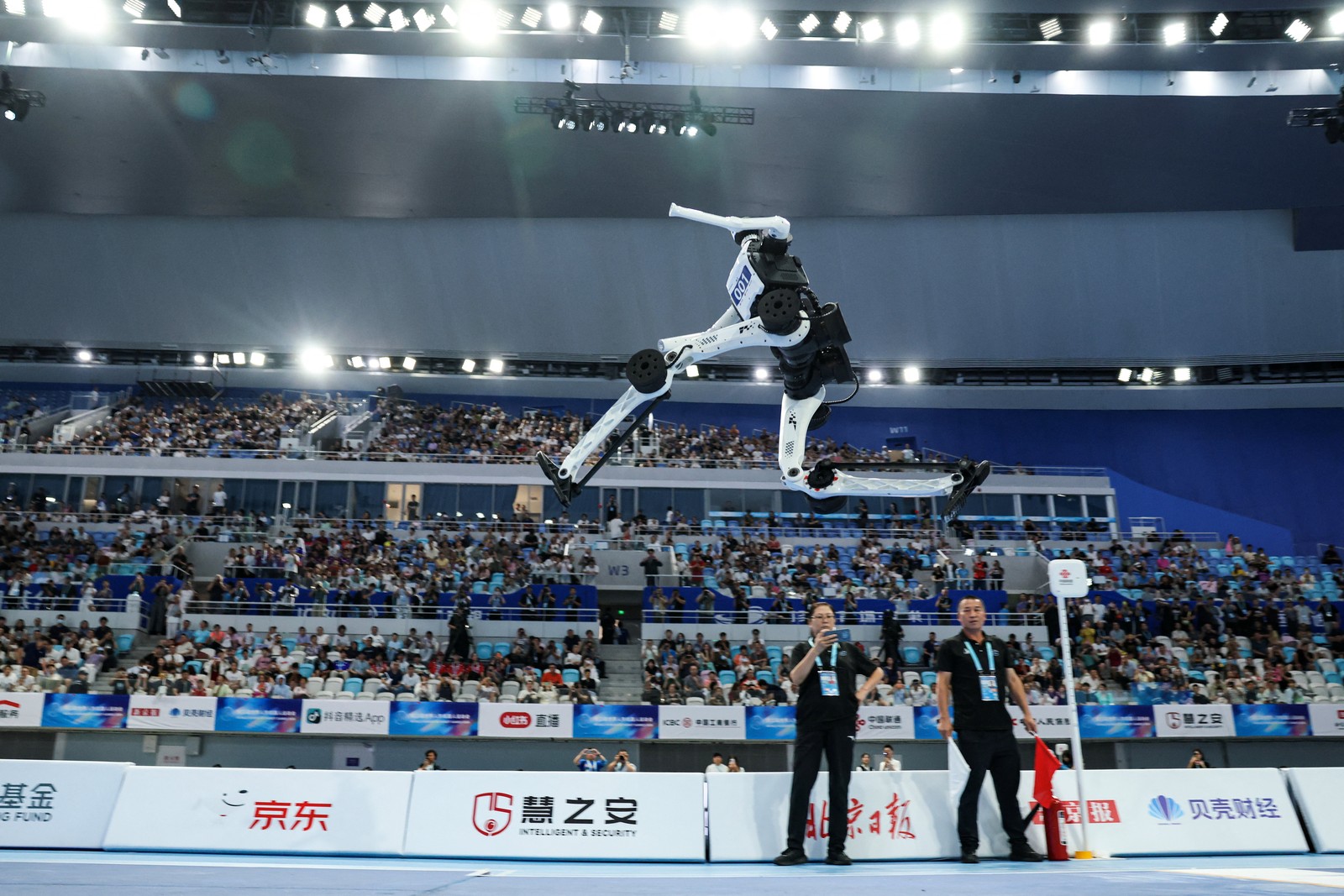 A low-angle view of a humanoid robot in midair during a long jump competition