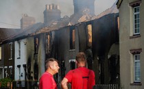 Two people stand in front of a burned building.