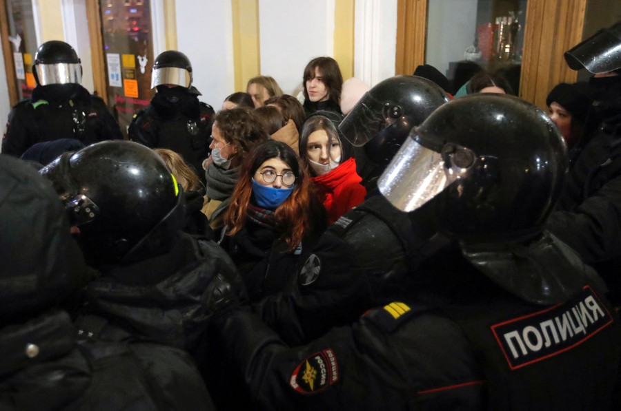 Police officers in riot gear surround a small crowd of anti-war protesters in Russia.