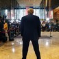 Trump stands, turned from the camera, hunched in front of a crowd of reporters