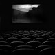 A black and white image of an empty movie theatre with a scenic location on screen