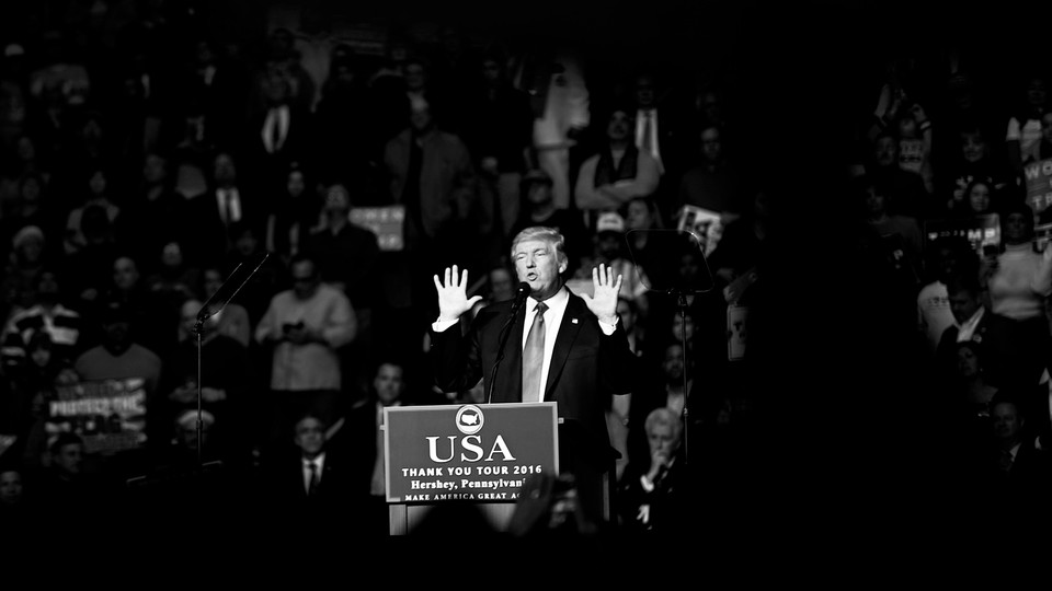 Black-and-white picture of Donald Trump speaking to a crowd from a podium with a sign that reads "USA THANK YOU TOUR 2016"