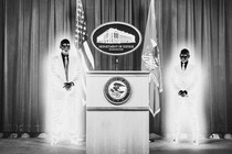 An illustration of two men in glowing suits standing near a Department of Justice lectern