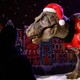 People look at an animated model of a Tyrannosaurus Rex wearing a Santa hat and festive sweater.
