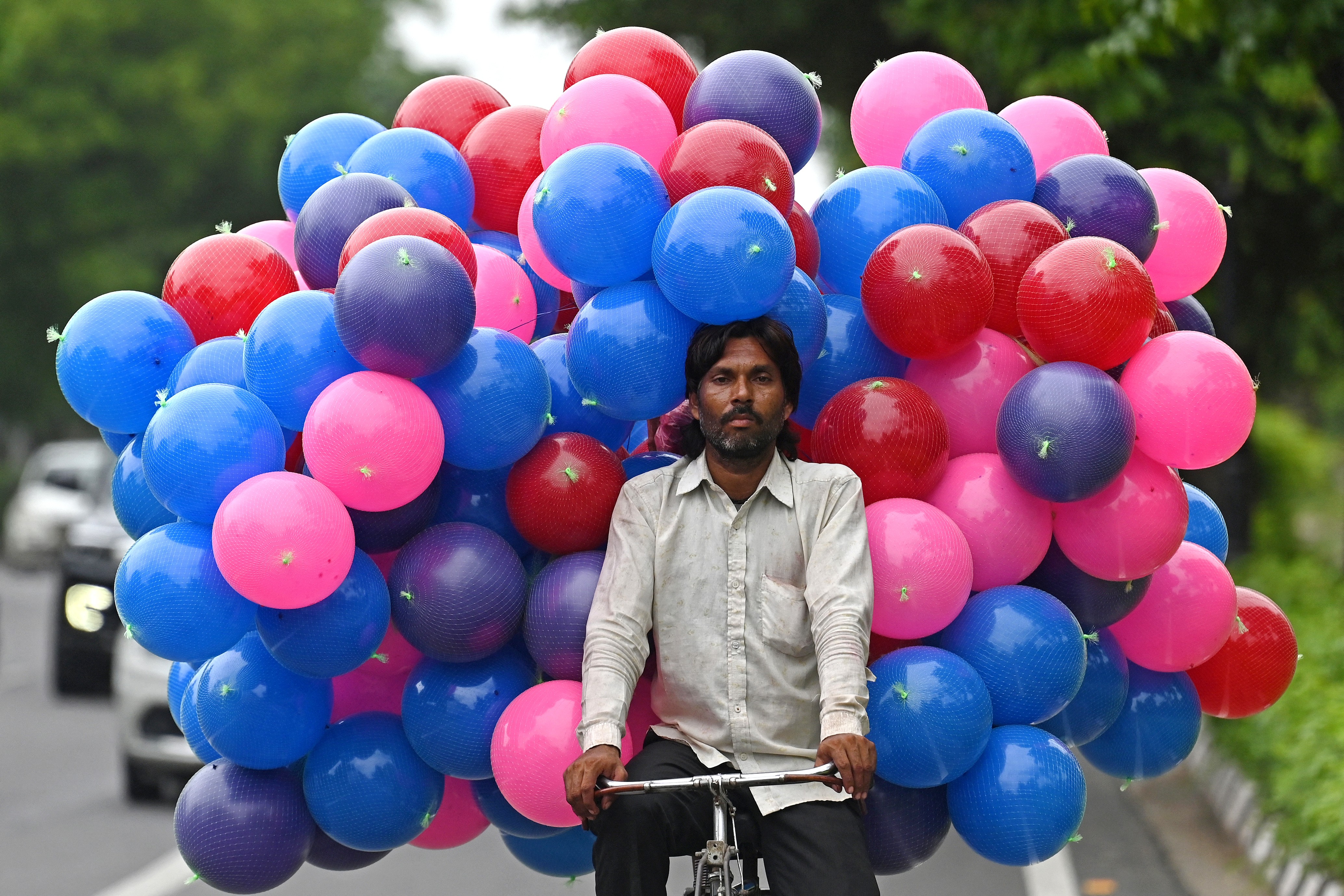 A vendor carries many plastic balls on a bicycle.