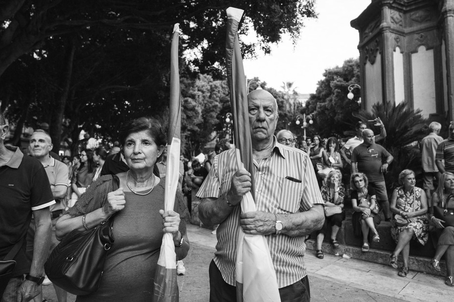 two Meloni stand with closed flags in their hands looking serious