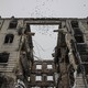 A flock of birds flies above the shell of a destroyed building.
