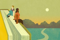 Two women sit atop a giant book, looking out at a sunset over a long road
