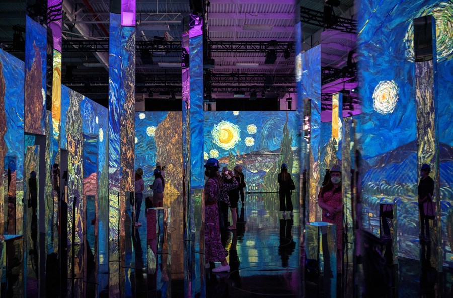 People walk among tall, brightly illuminated walls.