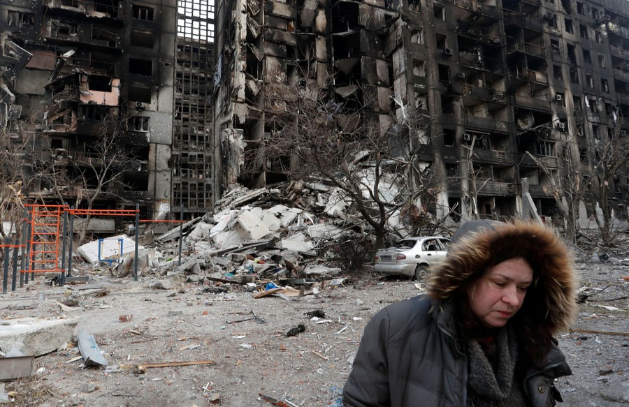 A woman walks outside a destroyed apartment building.