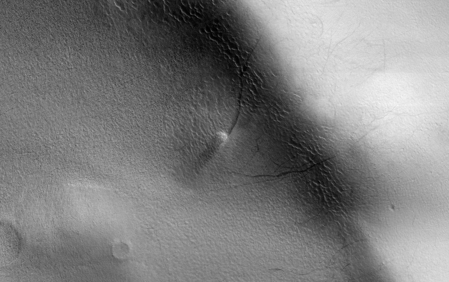 An orbital view of a small dust devil tracing a dark line across a dune.